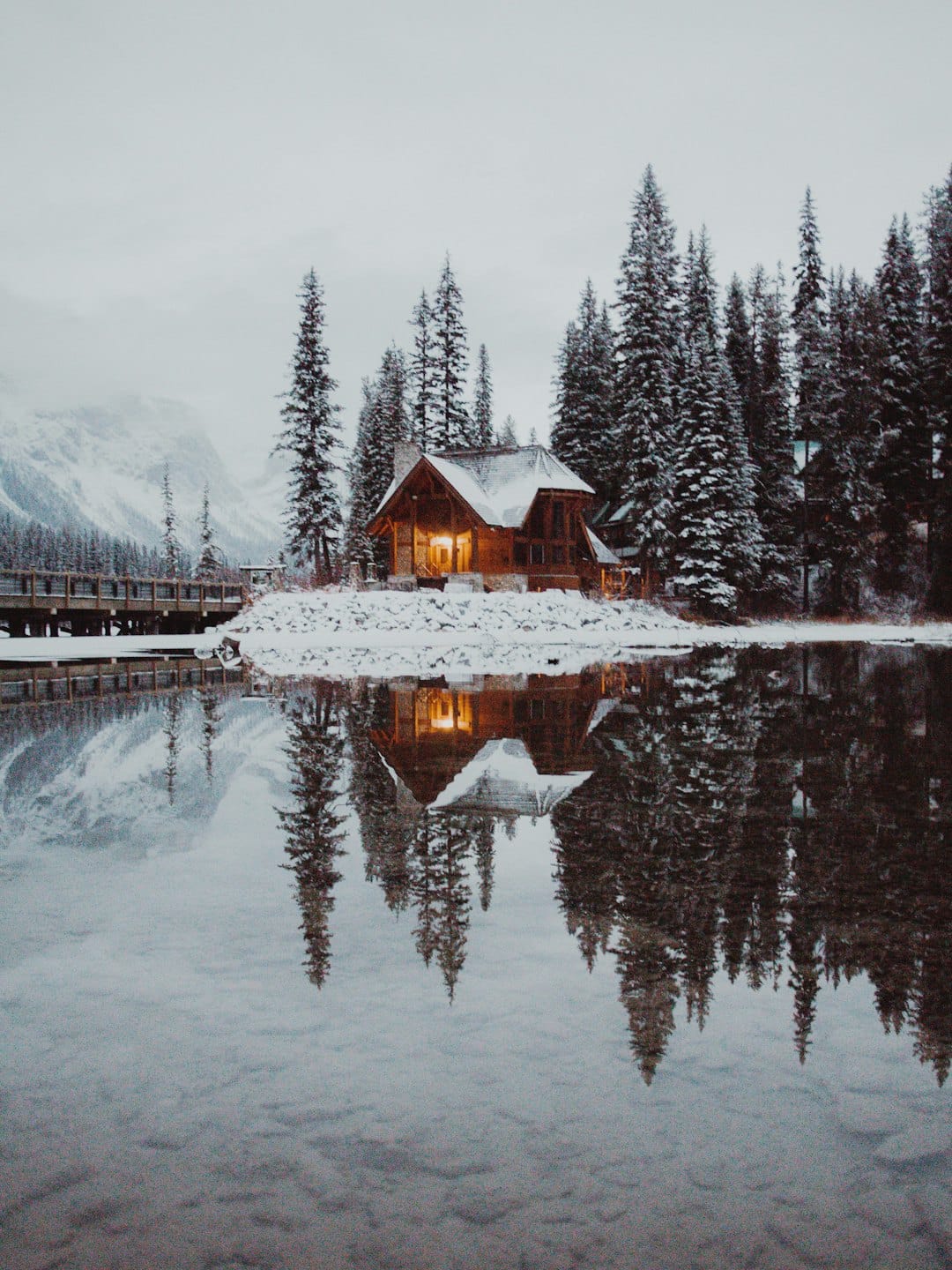 Een houten lodge weerspiegeld in een meer omringd door besneeuwde bomen.